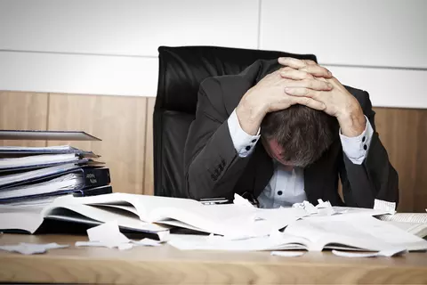 Man aan bureau kijkt naar beneden, met de handen op het hoofd
